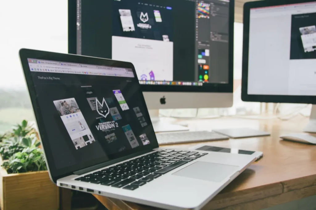 Meja kerja dengan laptop dan monitor menampilkan software desain