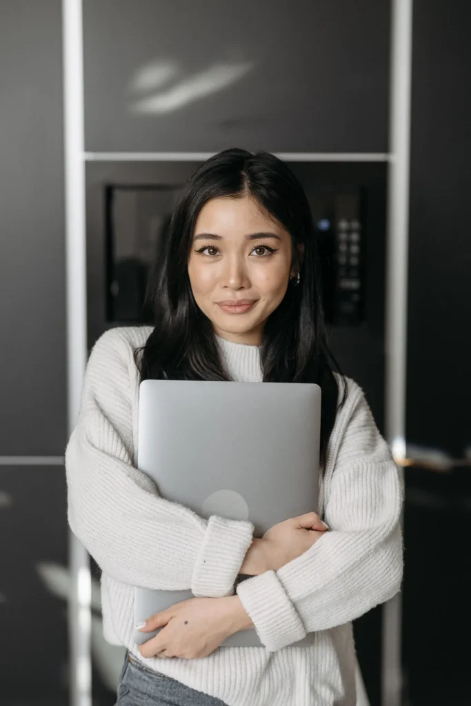 Membuat website tanpa coding, perempuan tersenyum memeluk laptop